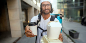 photo of a delivery person handing a coffee and some takeout food to someone, from the perspective of the customer