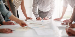 Low angle view of hands of multiracial group of people working with ideas and brainstorming together to make decisions with documents on table in creative office teamwork