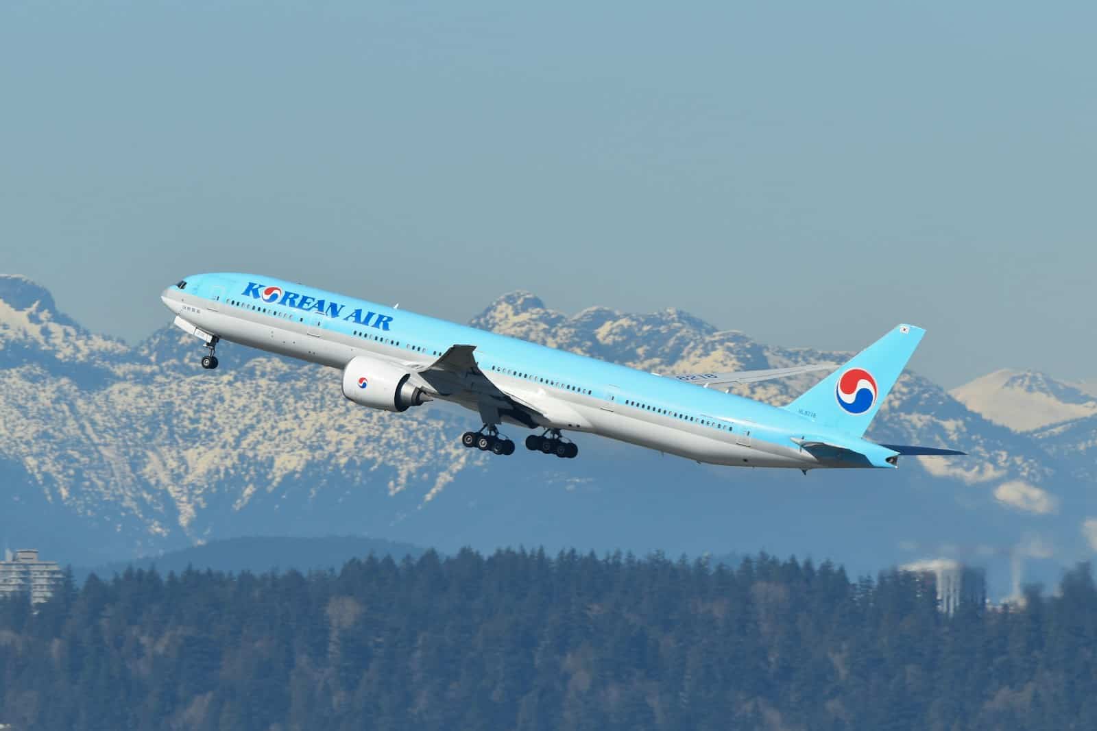 A blue and white airplane flying over a mountain range